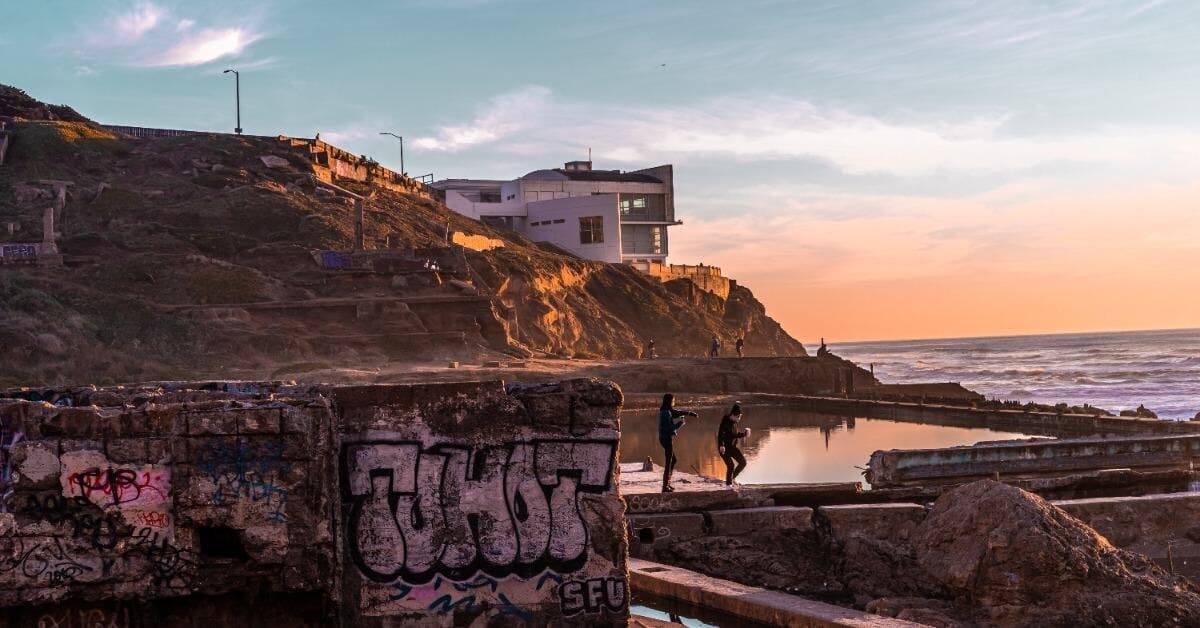 A tidal pool below a cliff at sunset, with warm light across the water.